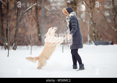 Picture of girl in black jacket playing with labrador at snowy park Stock Photo
