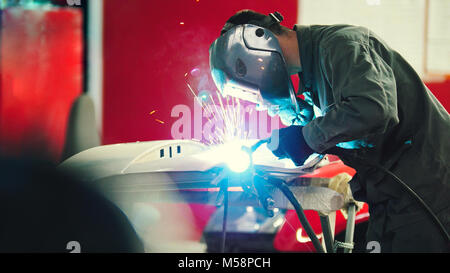 Welding industrial: worker in helmet repair detail in car auto service - blue sparklers Stock Photo