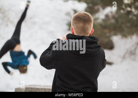 Teenager take a photo for acrobatic jump girl in winter city park - parkour concept Stock Photo