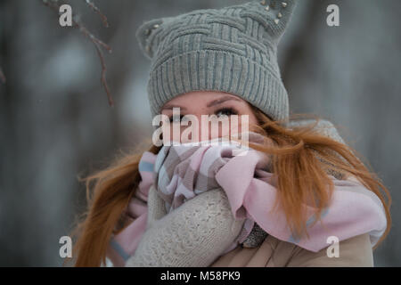 Portrait of young woman in winter park standing on alley, wrapped in a scarf Stock Photo