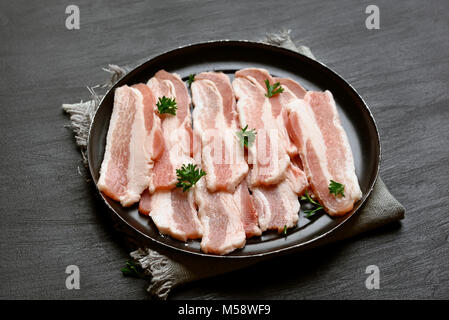 Bacon ready for cooking on black stone background, close up view Stock Photo