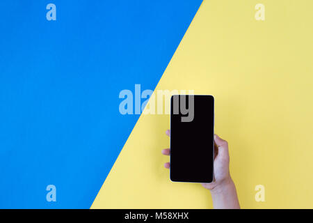 Hand holding the phone on blue and yellow background Stock Photo