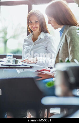 Happy young businesswoman with female colleague reading brochure at cafe table Stock Photo