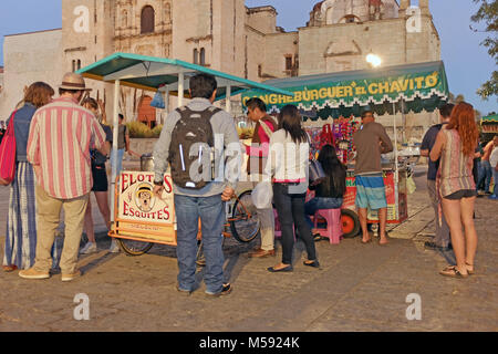 Backpacker travelers congregate around a food stand located in front of the Templo de Santo Domingo in the heart of Oaxaca, Mexico. Stock Photo