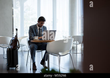 Businessman sitting in airport waiting area and working on laptop. Businessman at airport waiting lounge using laptop computer. Stock Photo