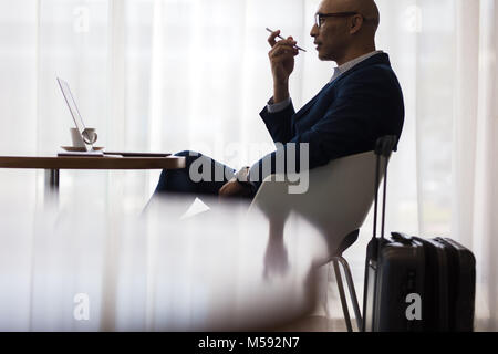 Businessman speaking on mobile phone while sitting at table in waiting lounge at airport. Male business traveler sitting at cafe inside airport with s Stock Photo
