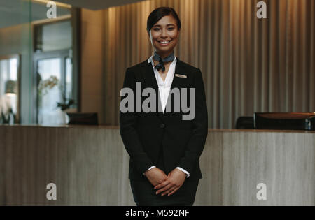 Happy smiling female receptionist in hotel. Beautiful concierge in uniform waiting for welcoming the guests. Stock Photo