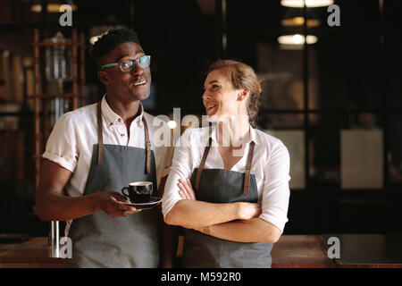 Happy coffee shop owner couple standing inside their shop. Man and woman baristas standing inside their café wearing apron. Stock Photo