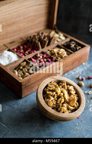 rustic wooden box full of oriental nuts, placed on gray table with wooden bowl full of walnuts Stock Photo