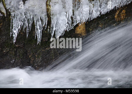 Waterfall rushing past a wall of sharp icicles Stock Photo