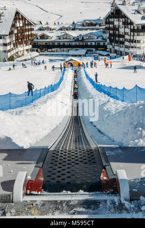 La Thuile, Italy - Feb 18, 2018: Ascending conveyor belt to a beginners run for children and parents in ski resort with mountains in background Stock Photo