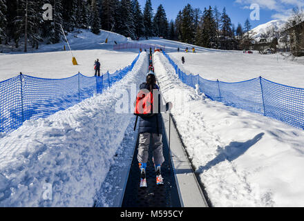 La Thuile, Italy - Feb 18, 2018: Ascending conveyor belt to a beginners run for children and parents in ski resort with mountains in background Stock Photo