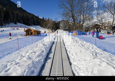 La Thuile, Italy - Feb 18, 2018: Ascending conveyor belt to a beginners run for children and parents in ski resort with mountains in background Stock Photo