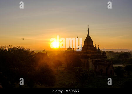 Hot-air balloons flying over the pagodas of Bagan and the foggy plains of the archaeological site during sunrise Stock Photo