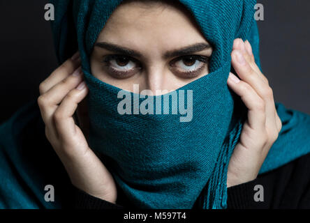 A Muslim girl with beautiful eyes is covered with a hijab. Arab woman on a black background. Stock Photo
