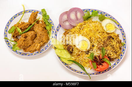 Popular Indian Mughlai cuisine of chicken biriyani (rice) and spicy mutton kosha (curry) with salad and sliced egg. Stock Photo