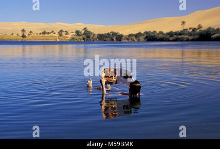 Libya. Ubari. Gabroun ( Gabrun) salt lake. Oasis. Ubari sandsea. Tourist reading magazine on Sahara desert, while floating in the water. Stock Photo