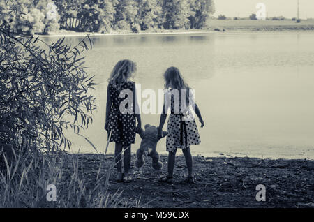 two little girls with long blond hair holding a teddy bear toy Stock Photo