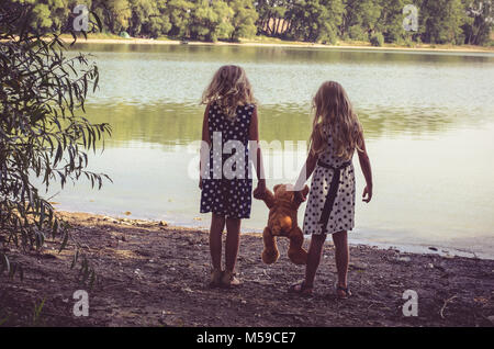 two little girls with long blond hair holding a teddy bear toy Stock Photo