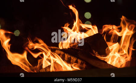 Fire in fireplace with firewood and colorful flames on black background. Close up with details, space. Stock Photo