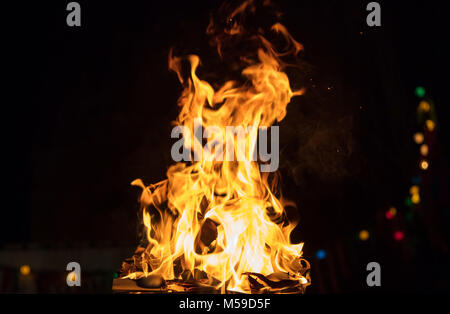 Fire in fireplace with firewood, colorful flames and bokeh lights. Big blaze on black blurred background. Close up view with details, space for text. Stock Photo