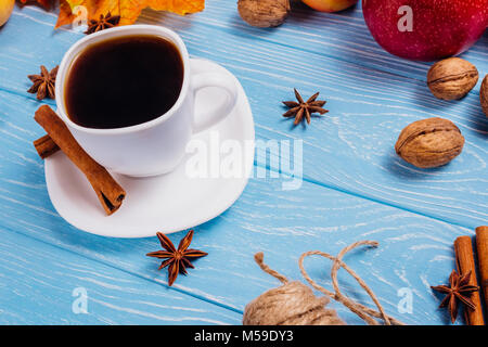White cup with black coffee on a blue wooden surface with anise and cinnamon sticks and walnuts Stock Photo