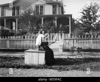 Mom and the children hang out in front of their Victorian home at the turn of the 20th century, ca. 1900. Stock Photo