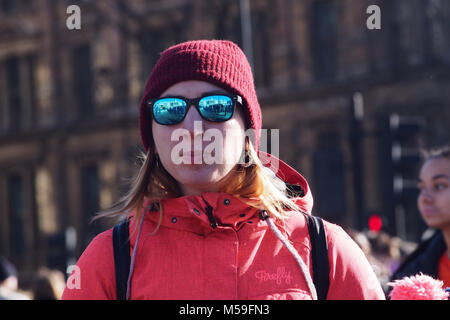 A woman wearing a red coat with a hood, a woolly hat and reflective, mirror sunglasses and carrying a backpack Stock Photo