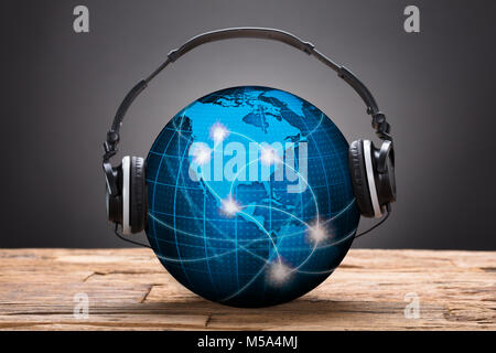 Closeup of headphones on blue globe against black background Stock Photo