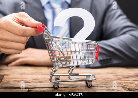 Midsection of businessman pushing question mark in shopping cart on wooden table Stock Photo