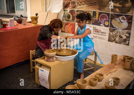 A female potter helping young girl to make clay pot on bending wheel in makeshift ceramic workshop at weekly market in La Bisbal d'Emporda, Baix Empor Stock Photo