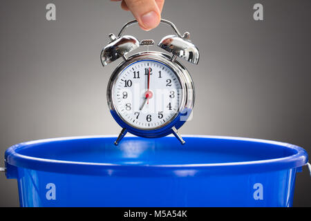 Cropped hand of businessman throwing alarm clock in blue bucket against gray background Stock Photo