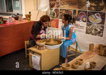 A female potter helping young girl to make clay pot on bending wheel in makeshift ceramic workshop at weekly market in La Bisbal d'Emporda, Baix Empor Stock Photo