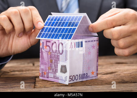 Businessman installing solar panels on house made from  euro papernotes on wooden table Stock Photo