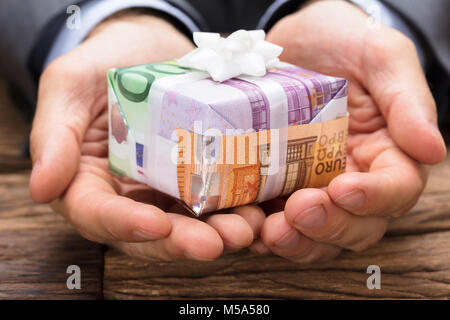 Cropped image of businessman holding gift box made from euro papernotes at wooden table Stock Photo