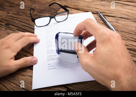 Cropped hands of businessman stamping contract paper at wooden table Stock Photo