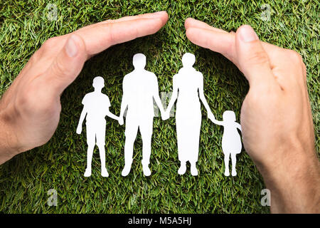 Directly above shot of businessman's hands covering paper family on grass Stock Photo