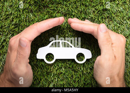 Directly above shot of businessman's hands covering paper car on grass Stock Photo