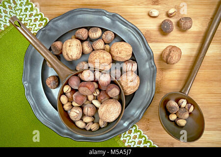 Nuts of various kinds on a metal plate, from above on a wooden board Stock Photo