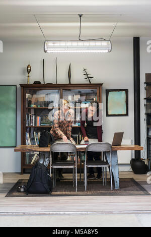 Two women gathered around table in office area of a metal workshop, looking at technical blueprint. Stock Photo