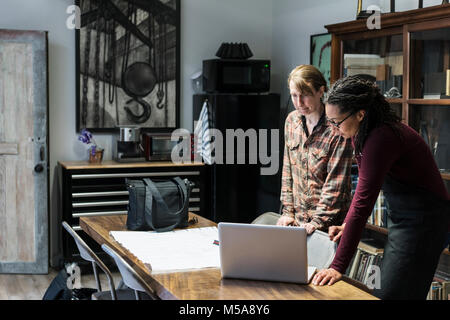 Two women gathered around table in office area of a metal workshop, looking at laptop. Stock Photo