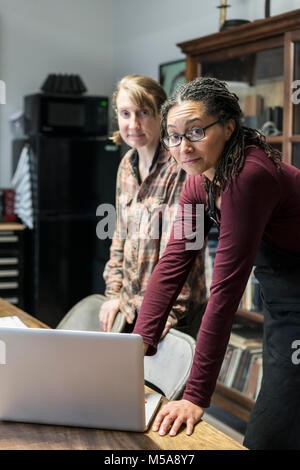 Two women gathered around table in office area of a metal workshop, looking at laptop. Stock Photo