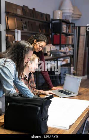 Three women gathered around table in office area of a metal workshop. Stock Photo