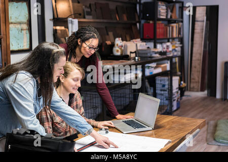 Three women gathered around table in office area of a metal workshop. Stock Photo