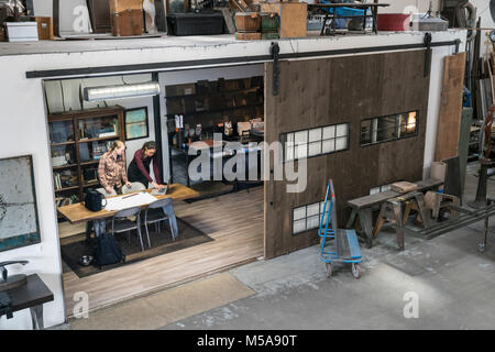 High angle view of two women gathered around table in office area of metal workshop. Stock Photo