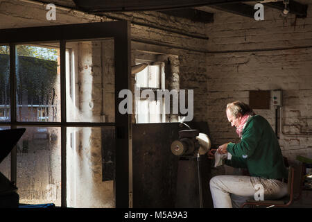 A craftsman sitting in a workshop sharpening the blade of a knife using a surface grinder. Stock Photo