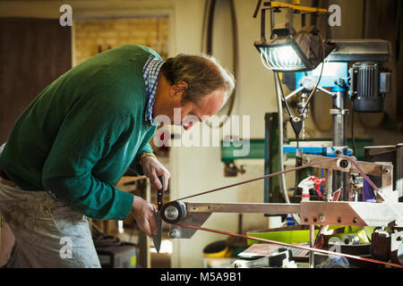 A craftsman in a workshop, holding a knife and smoothing and finishing a handle with a sanding wheel. Stock Photo