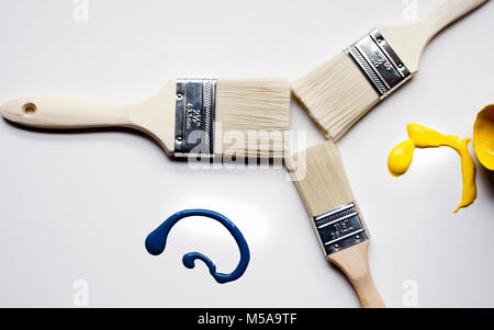 Three paint brushes laid out on canvas with two different colour splashes Stock Photo