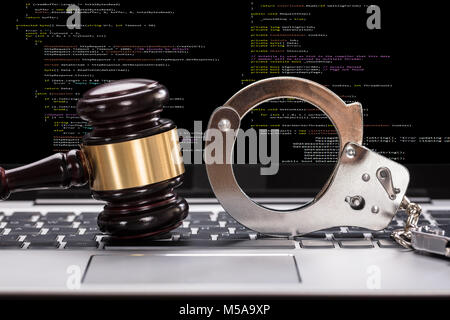 Close-up Of Handcuffs And Gavel In Front Of Laptop Screen Stock Photo
