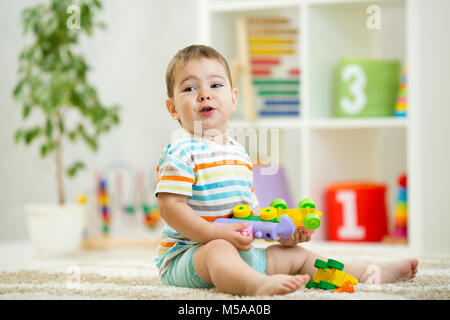 Happy child playing with colorful plastic bricks on the floor. Toddler having fun and building a train out of constructor bricks. Early learning. Developing toys Stock Photo